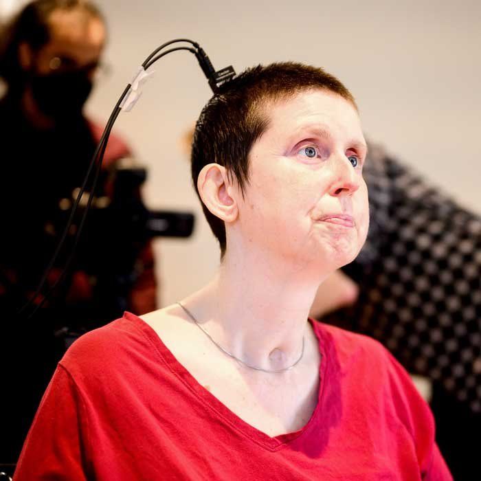 A white woman with close-cropped hair and a small brain monitor on wearing a red shirt