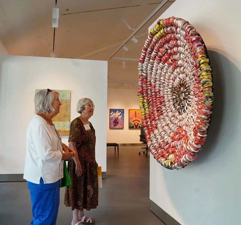 Two women look at a large circular piece of art in a museum gallery.
