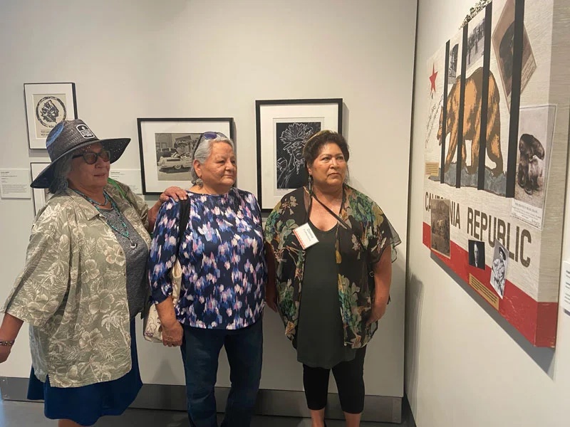Three women look at a piece of art based on the California bear flag