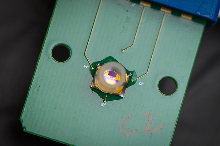 Close-up image of a biosensor, a green slat with a hole on the left and ride sides, with three wires stuck to the surface, leading to a central hub with a plastic ring