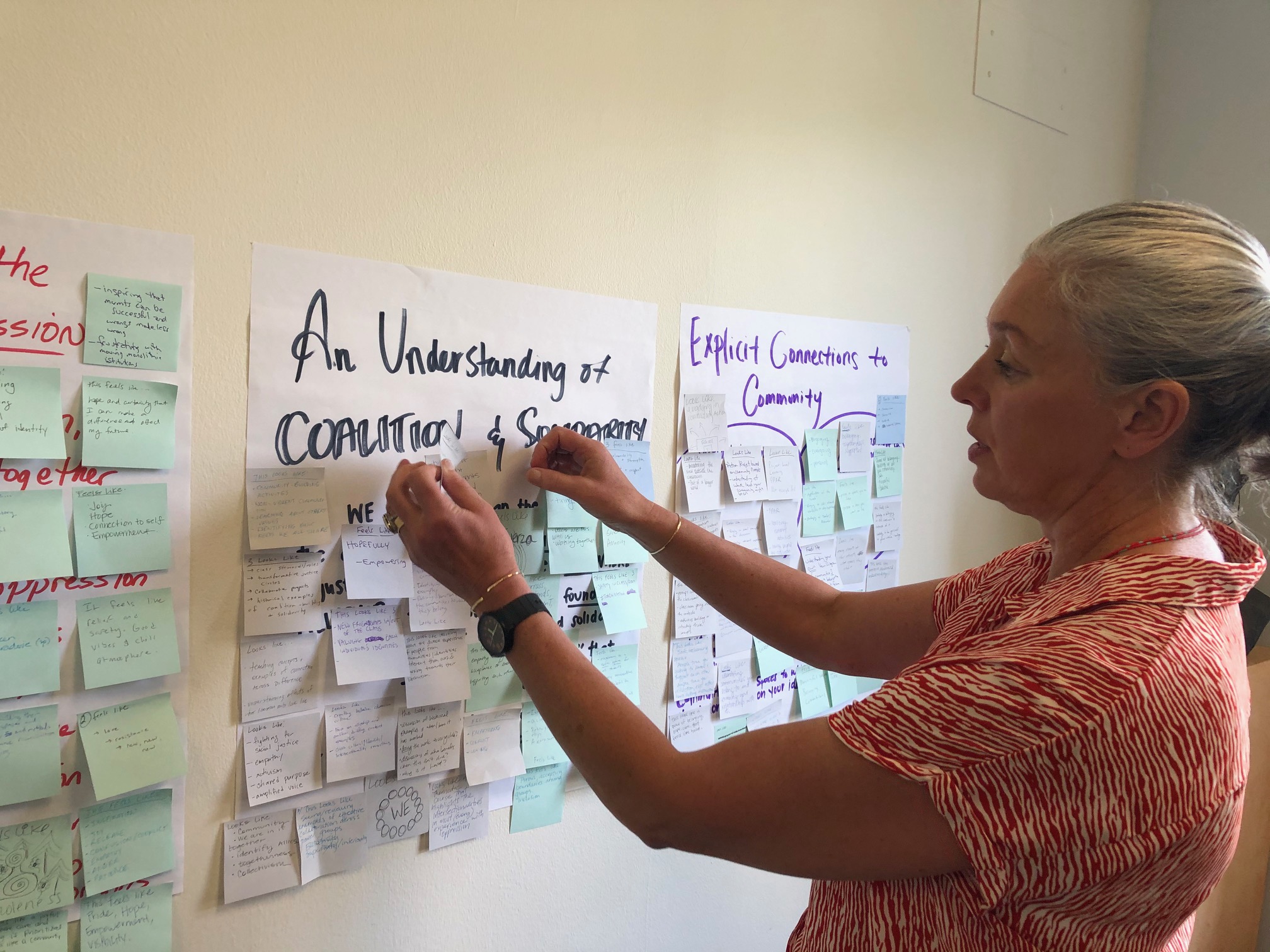 White woman putting sticky notes on a board that says An Understanding of Coalition