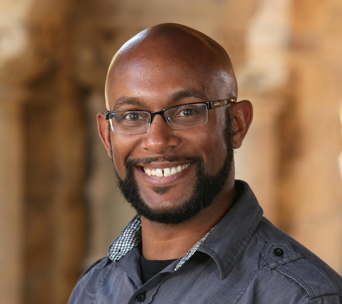 Smiling bald Black male educator with a beard and glasses