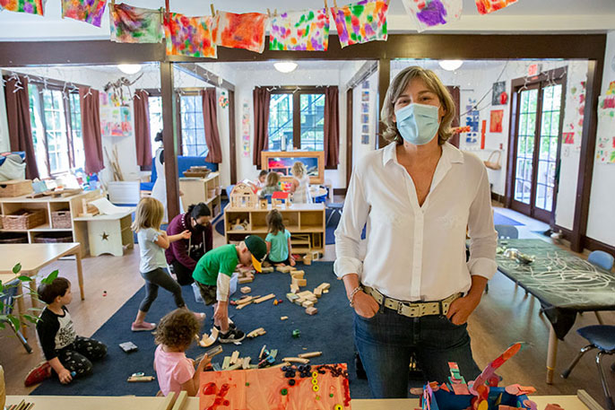 Rockridge Little School owner Holly Gold stands in a classroom with a teacher and busy preschool children