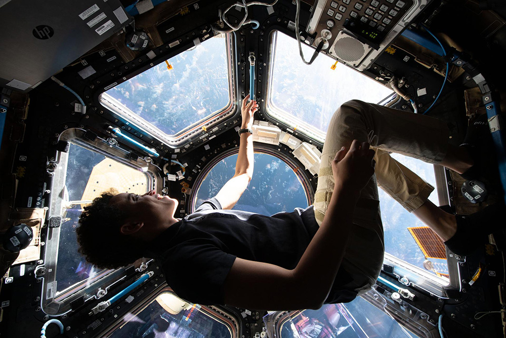 Jessica Watkins floats in the cupola of the International Space Station wearing a blue shirt and khakis