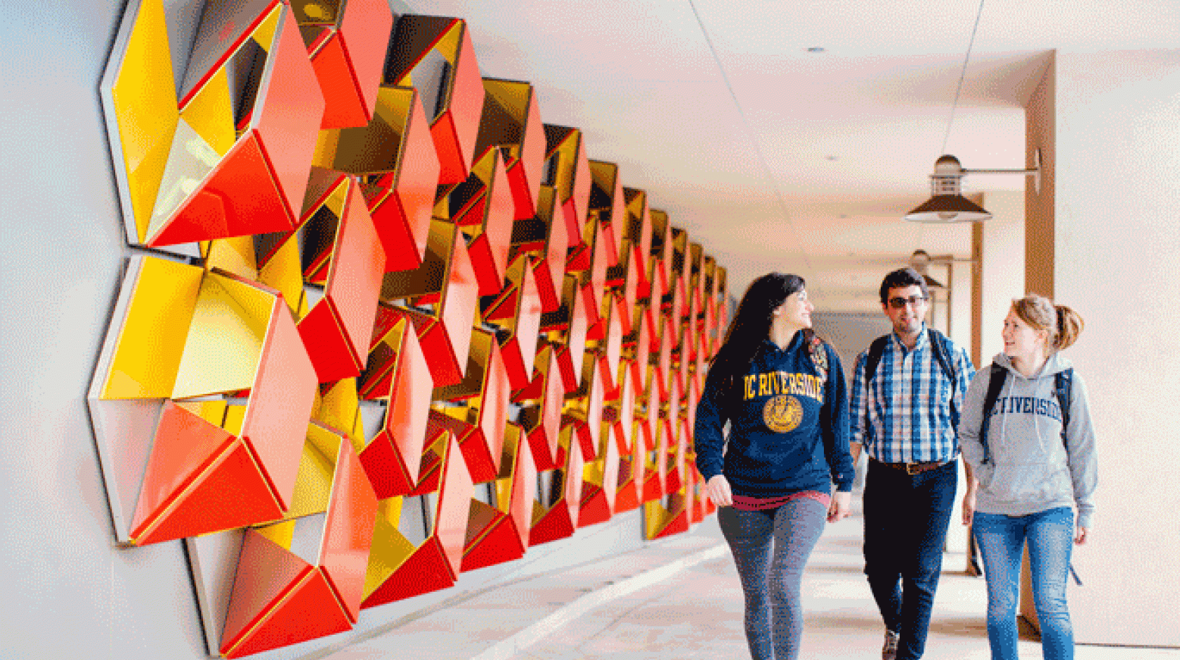 Three students walking a colorful UC Riverside hallway