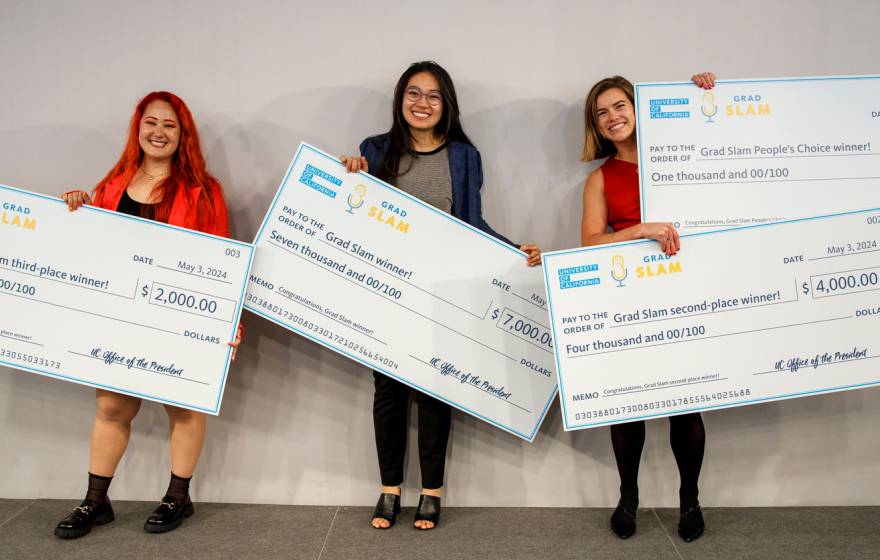 Three people standing holding giant checks