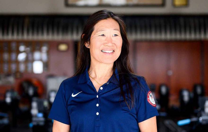 Dr. Cindy Chang poses for a portrait in front of a set of exercise equipment. In the background is a framed Olympic flag.