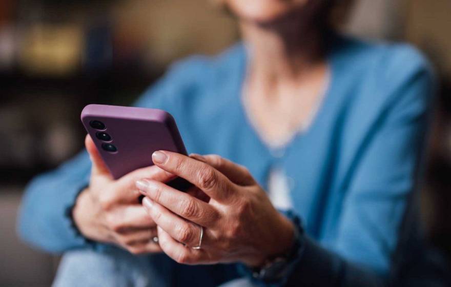 Senior woman uses smartphone; smartphone is central to image, woman's face is cropped out and body blurred
