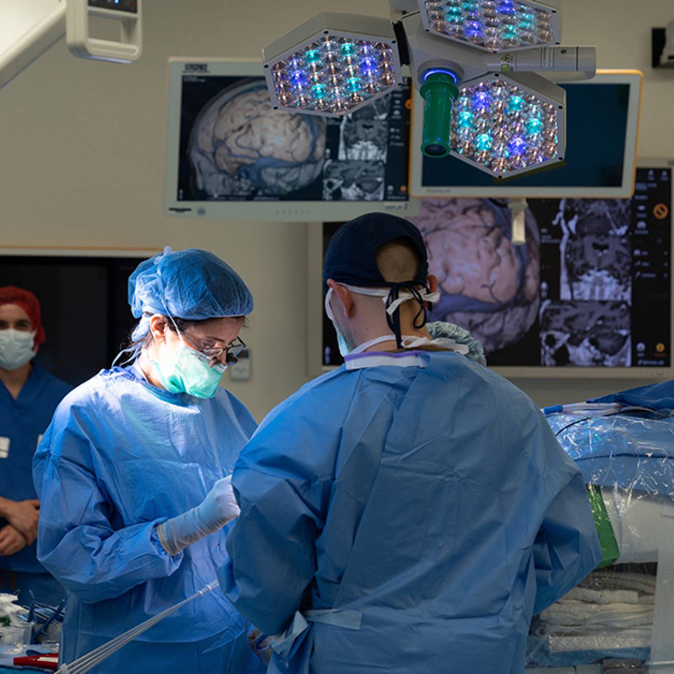 Surgeons operating in an operating room with brain scans hanging around the theater