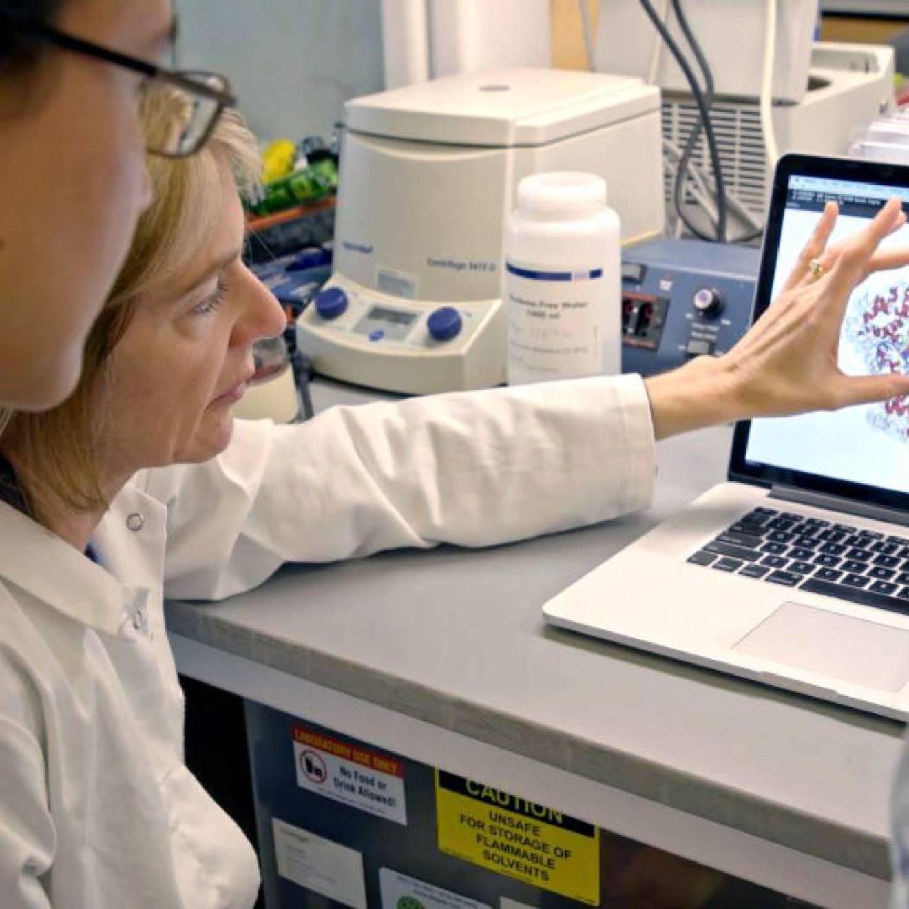 CRISPR research A woman doctor in a lab coat shows a male student a molecule on a computer