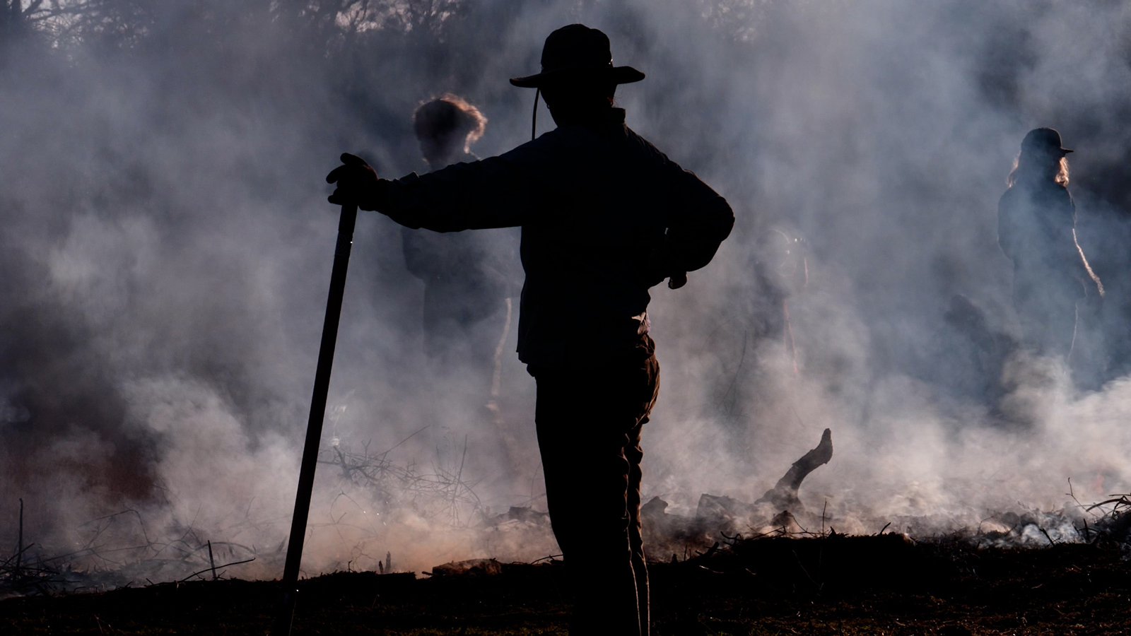 A person standing in the middle of raking coals after a cultural burn