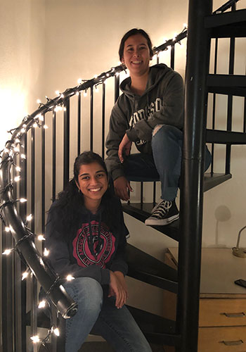 Anjika Pai and her best friend Hannah Young sit on a spiral staircase wrapped with tiny lights together
