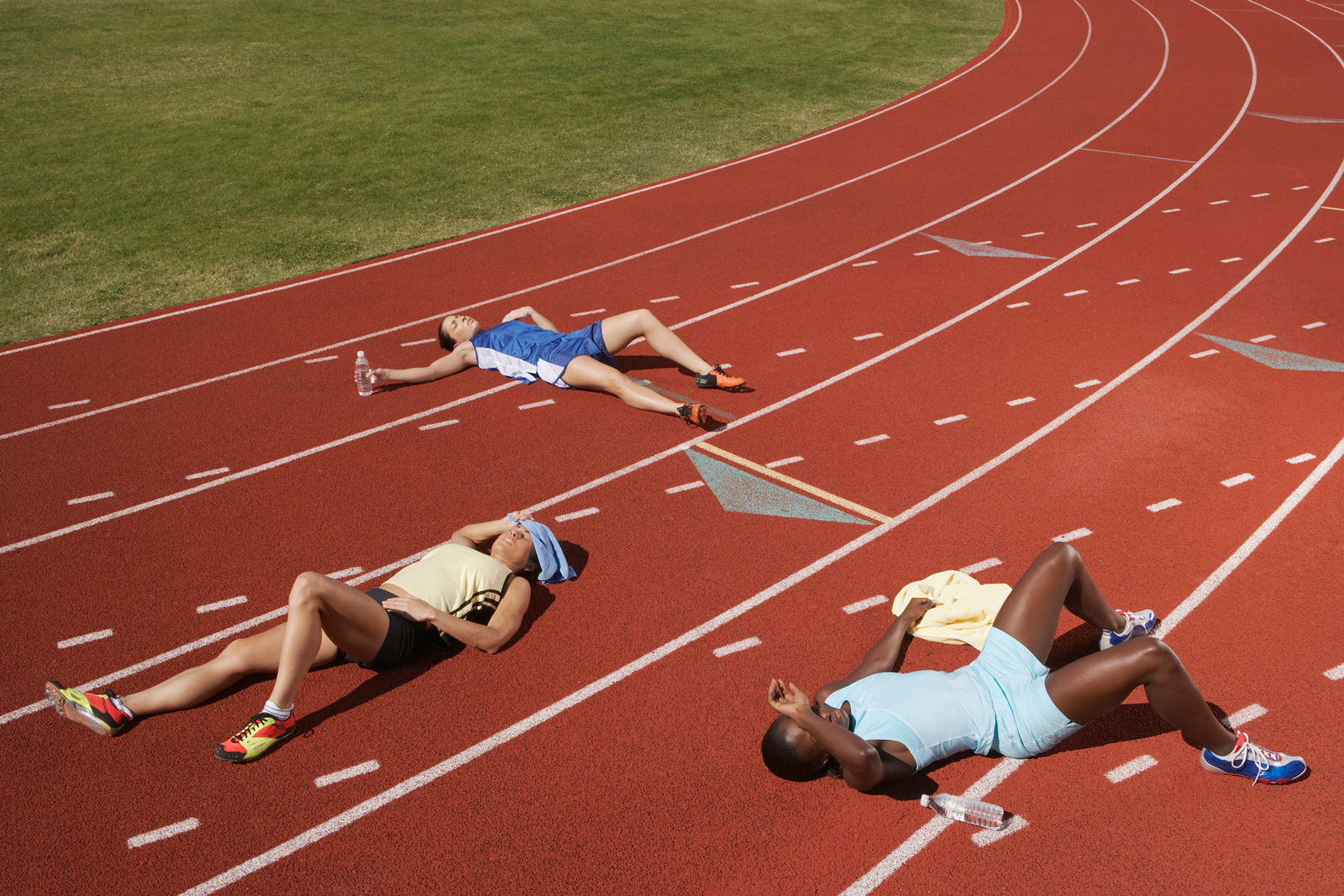 Three runners lying down on a track in a track-and-field area