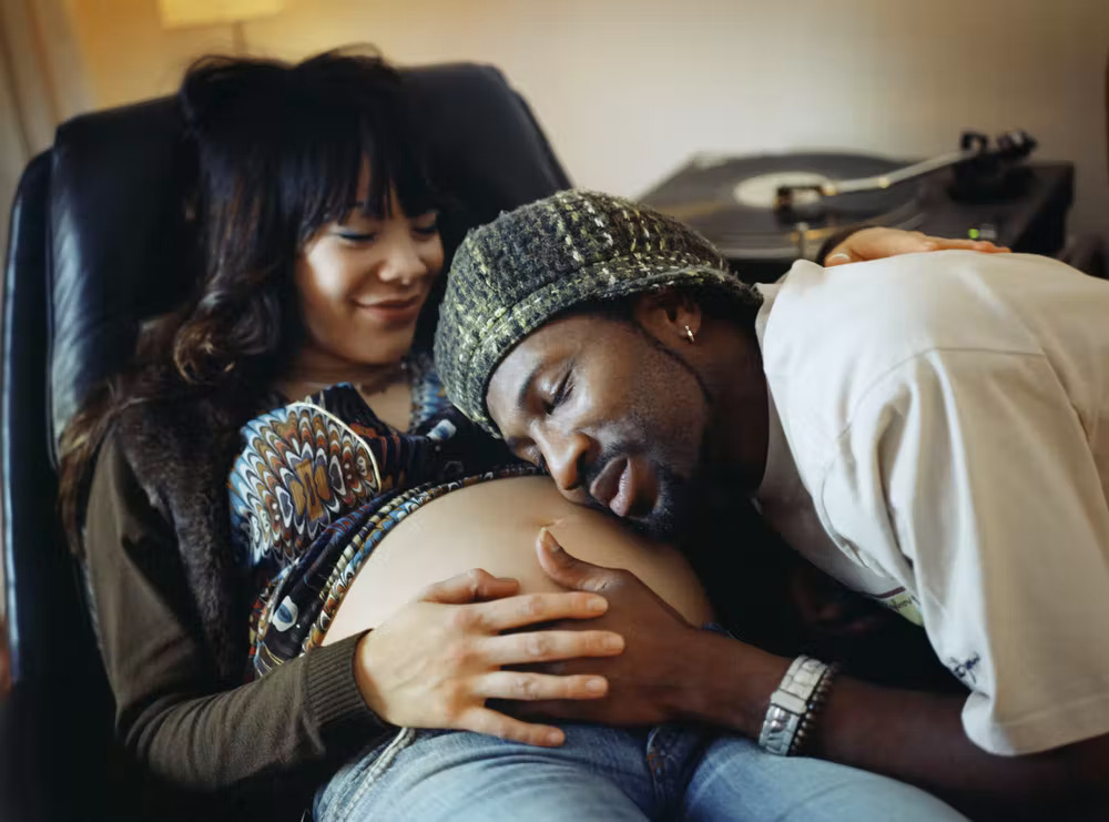 Black man listens to Black pregnant woman's belly