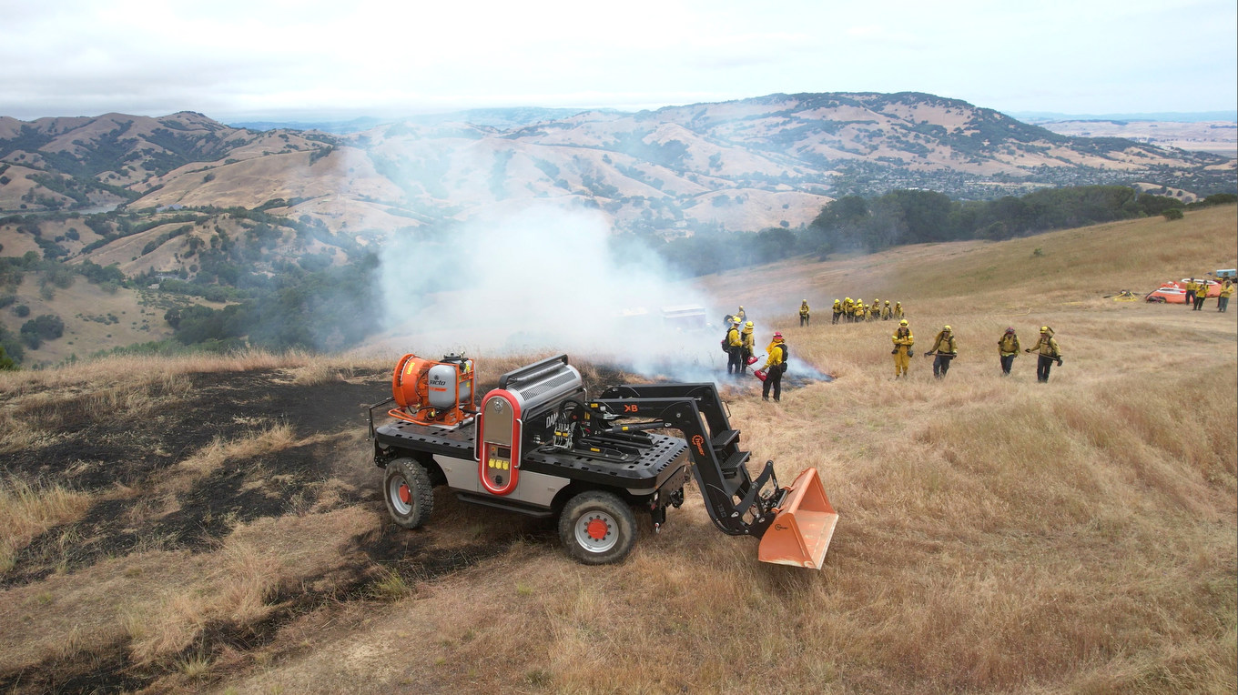 A utility vehicle with plow, firefighters behind in distance