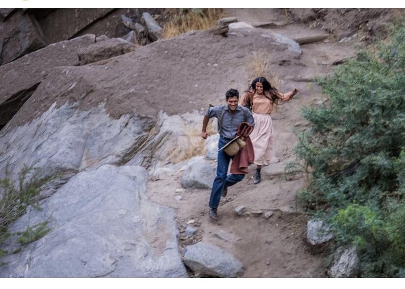 A young Native American man running down a rocky slope with a young Native American woman