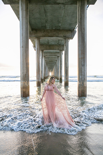Michelle, smiling, in a flowing dress underneath a pier