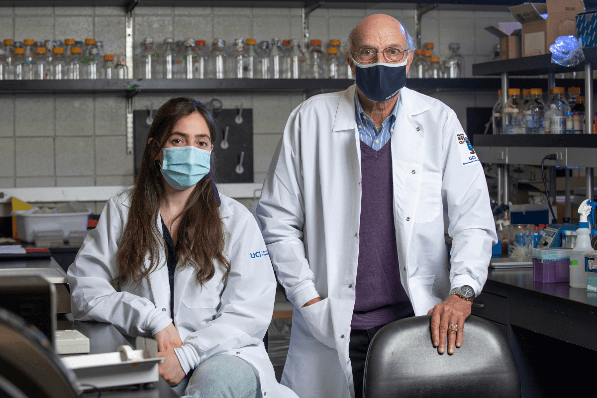 A young woman and an older man in a lab wearing PPE