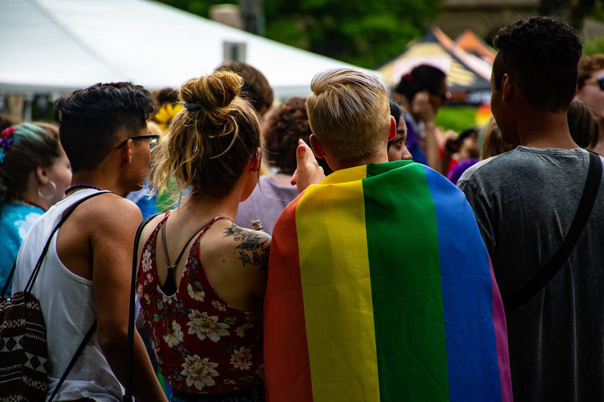 Teens at a rally, one wearing a Pride flag