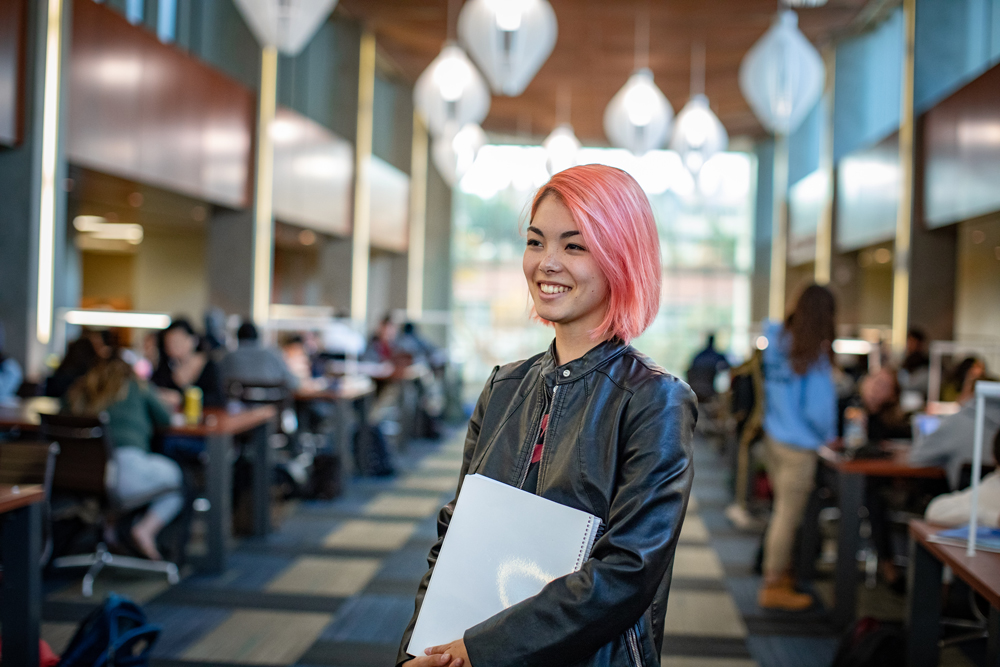 Young woman with pink hair holding a computer and smiling