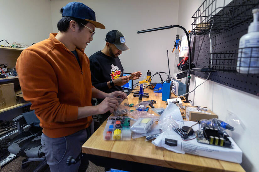 Two men working at a table with small plastic pieces of equipment