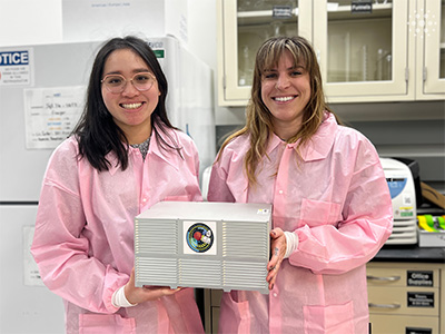 Two women in pink protective wear holding a box
