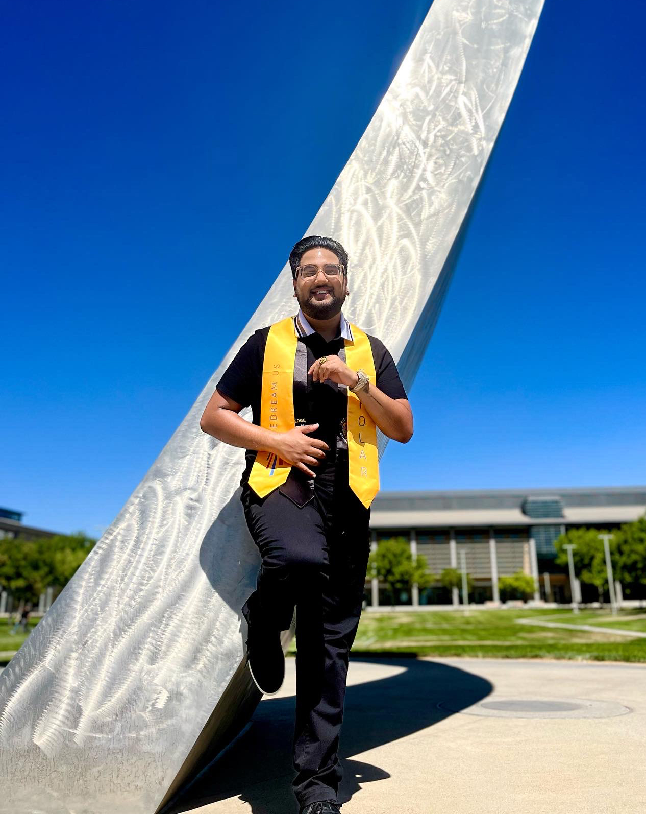 Josiah Beharry leans against the UC Merced arch wearing a yellow graduation stole