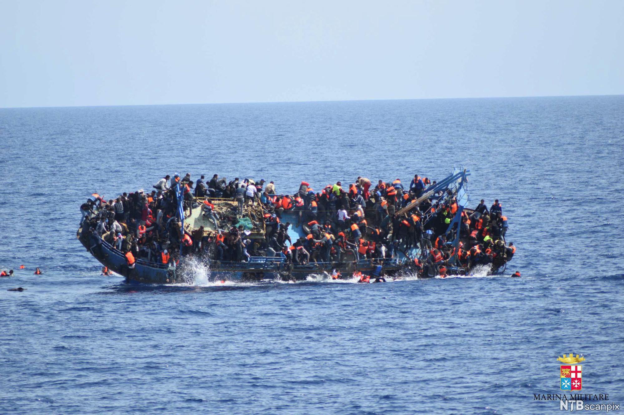 A boat filled with people capsizing in open ocean