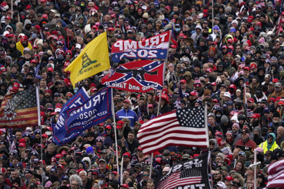A large crowd in Washington DC. In the foreground are five flags: the American Flag, 2 Trump campaign flags, the Don't Tread On Me Flag, and a Confederate flag.