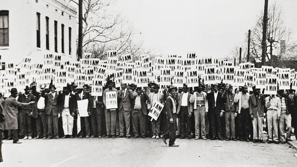 Black and white image of maybe 100 Black men holding signs reading "I AM A MAN"