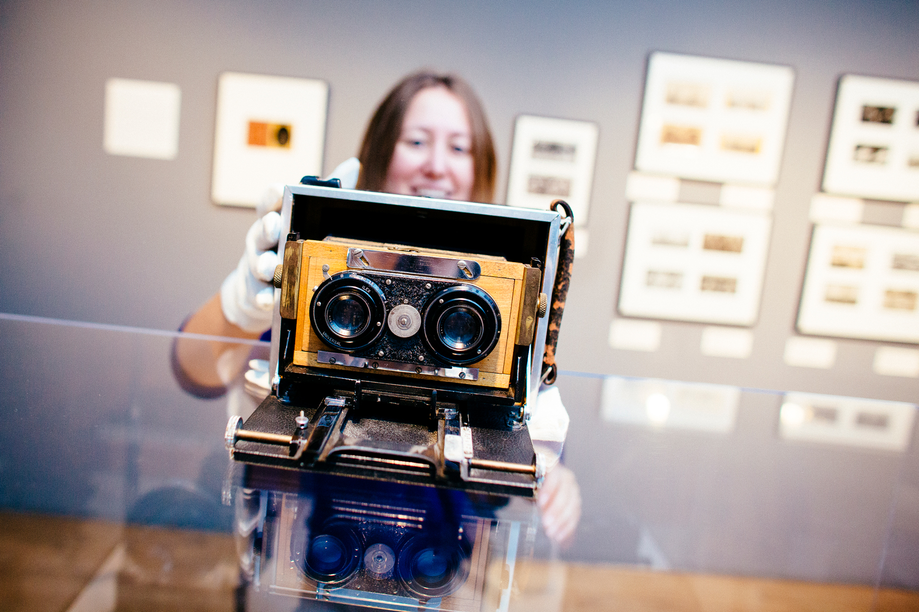 A person wearing white gloves holds an old camera in a museum gallery