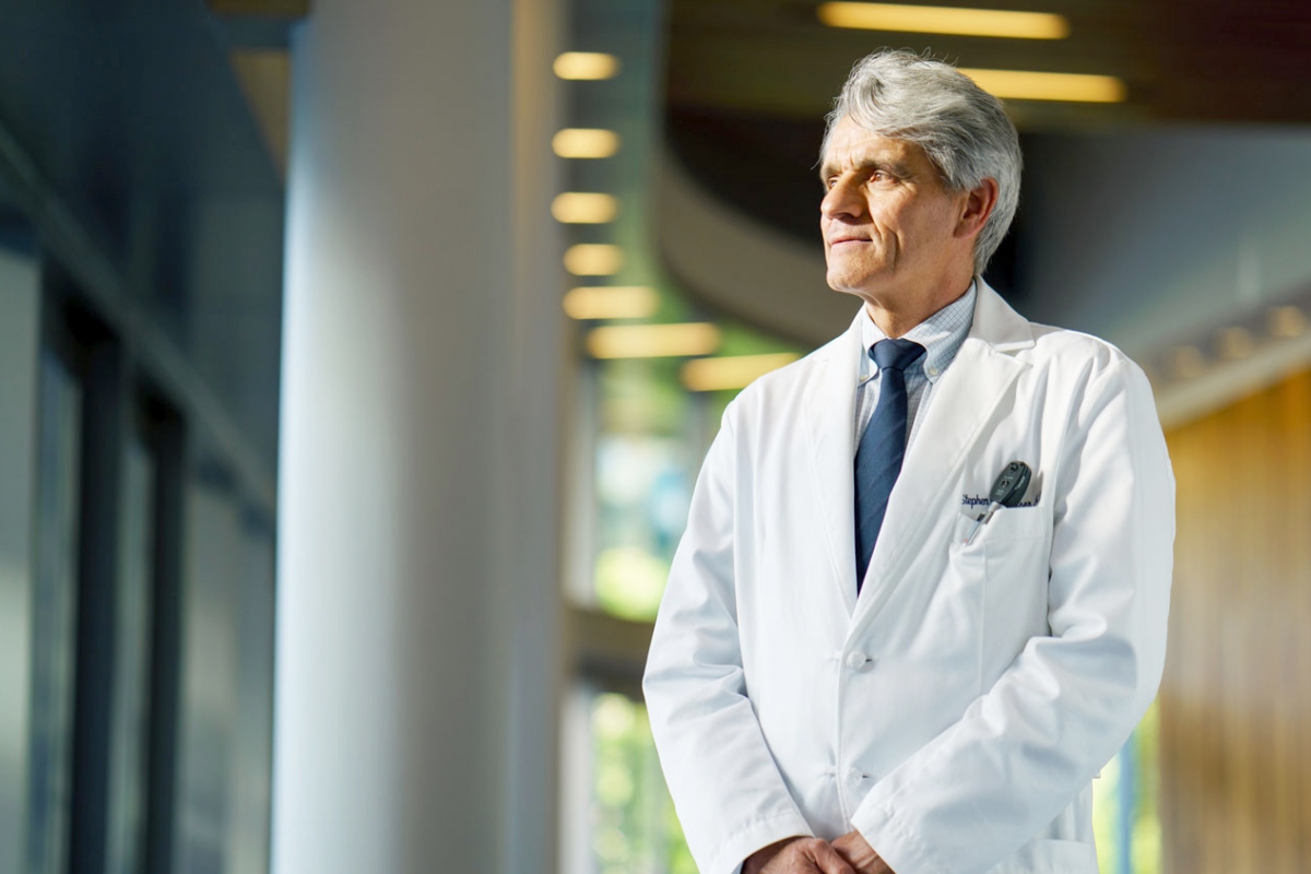 A man with white hair in a medical coat and a blue tie stares pensively within a UCSF building