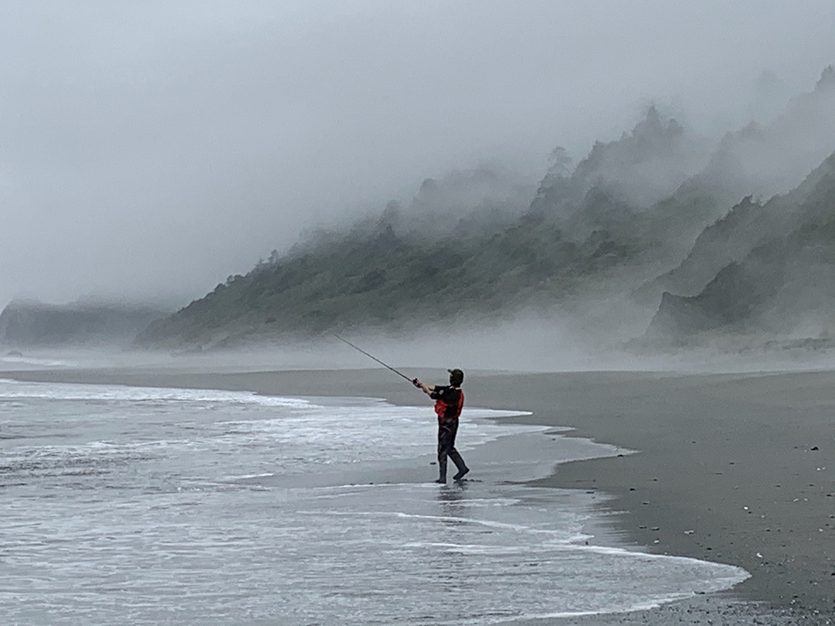 A person fishing on the beach with foggy mountains in the background