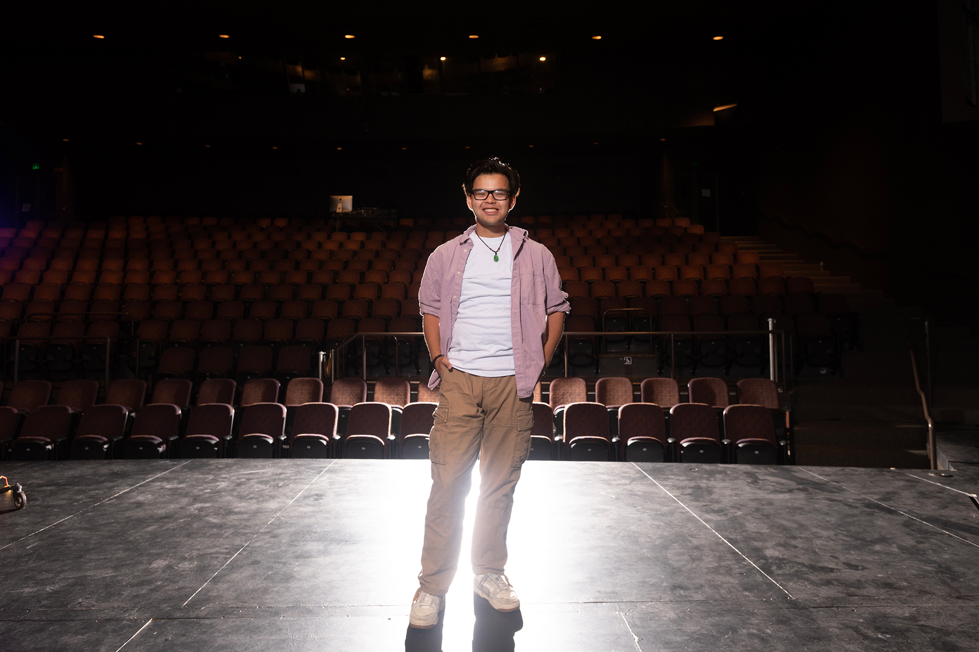 Young man smiles under the spotlight on an empty stage, seats behind him