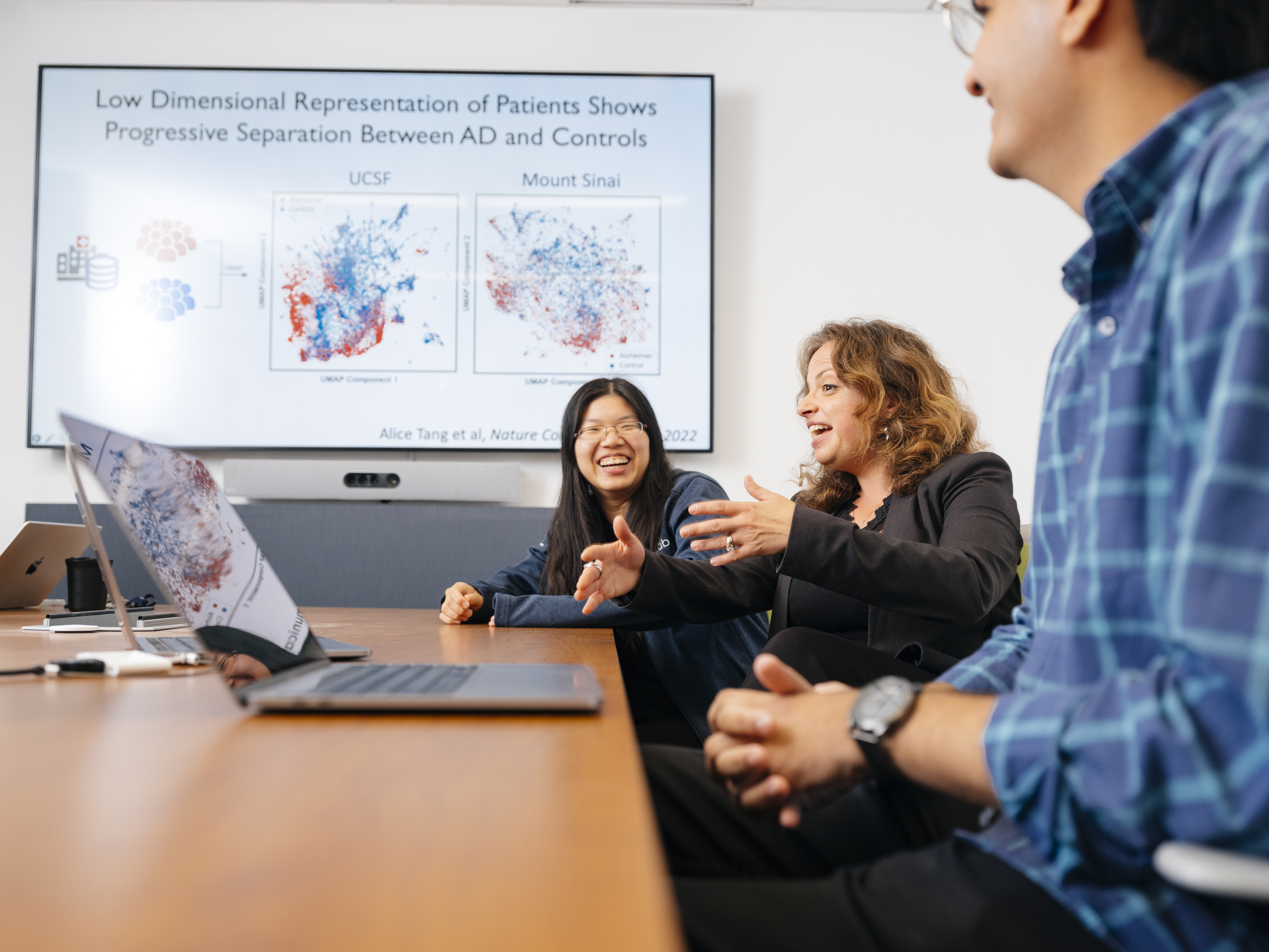 Alice Tang, Marina Sirota and another member of their lab discuss a research presentation in a conference room.