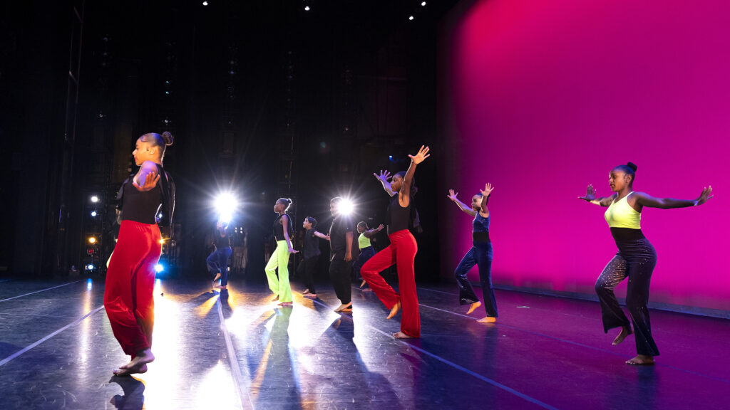 Six student dancers perform on stage against a glowing pink curtain