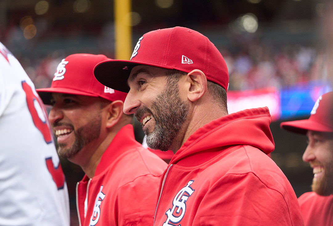 Daniel Descalso in profile, on the bench at a MLB game wearing St. Louis Cardinals attire, smiling