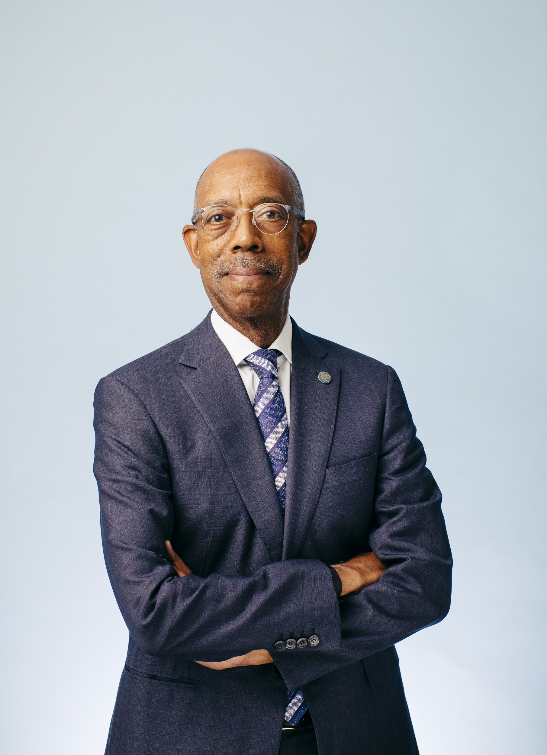 Michael V. Drake, M.D., smiling man with glasses, in a navy suit, arms folded