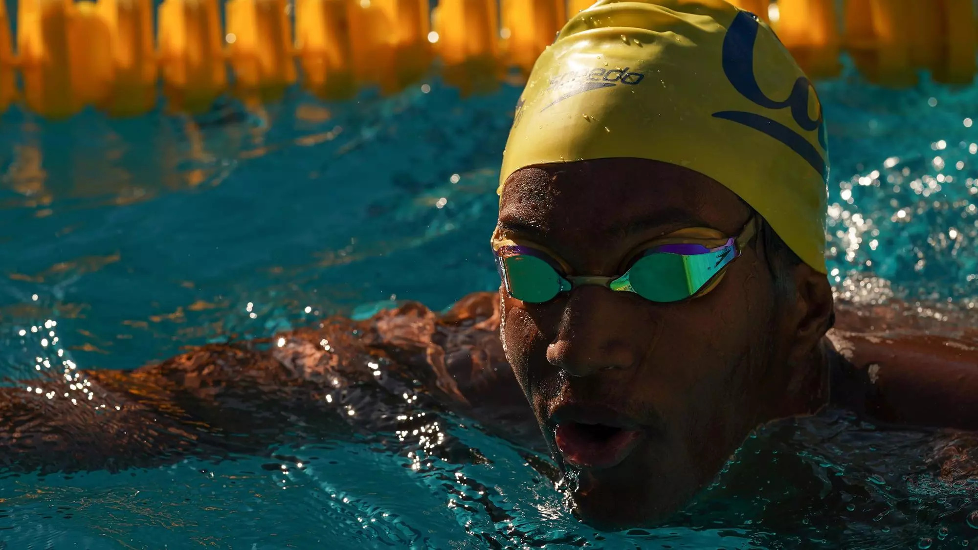 Young Black man mid-swim in a Cal swim cap with goggles