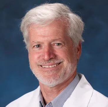 White man with white hair, white beard, white medical coat, smiling in portrait