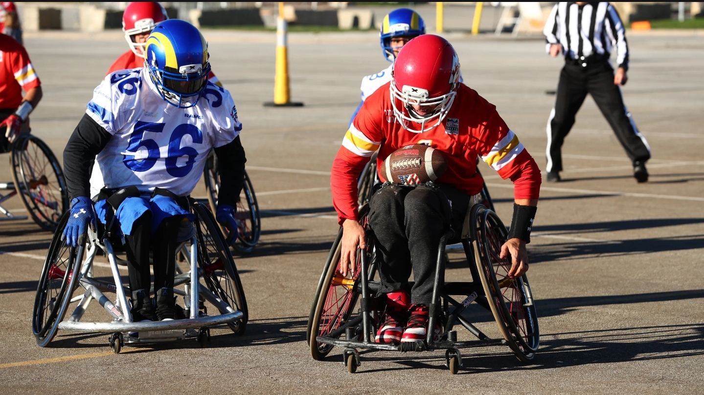 A wheelchair football player for the LA Rams pursues a Kansas City Chiefs wheelchair football player who has the ball