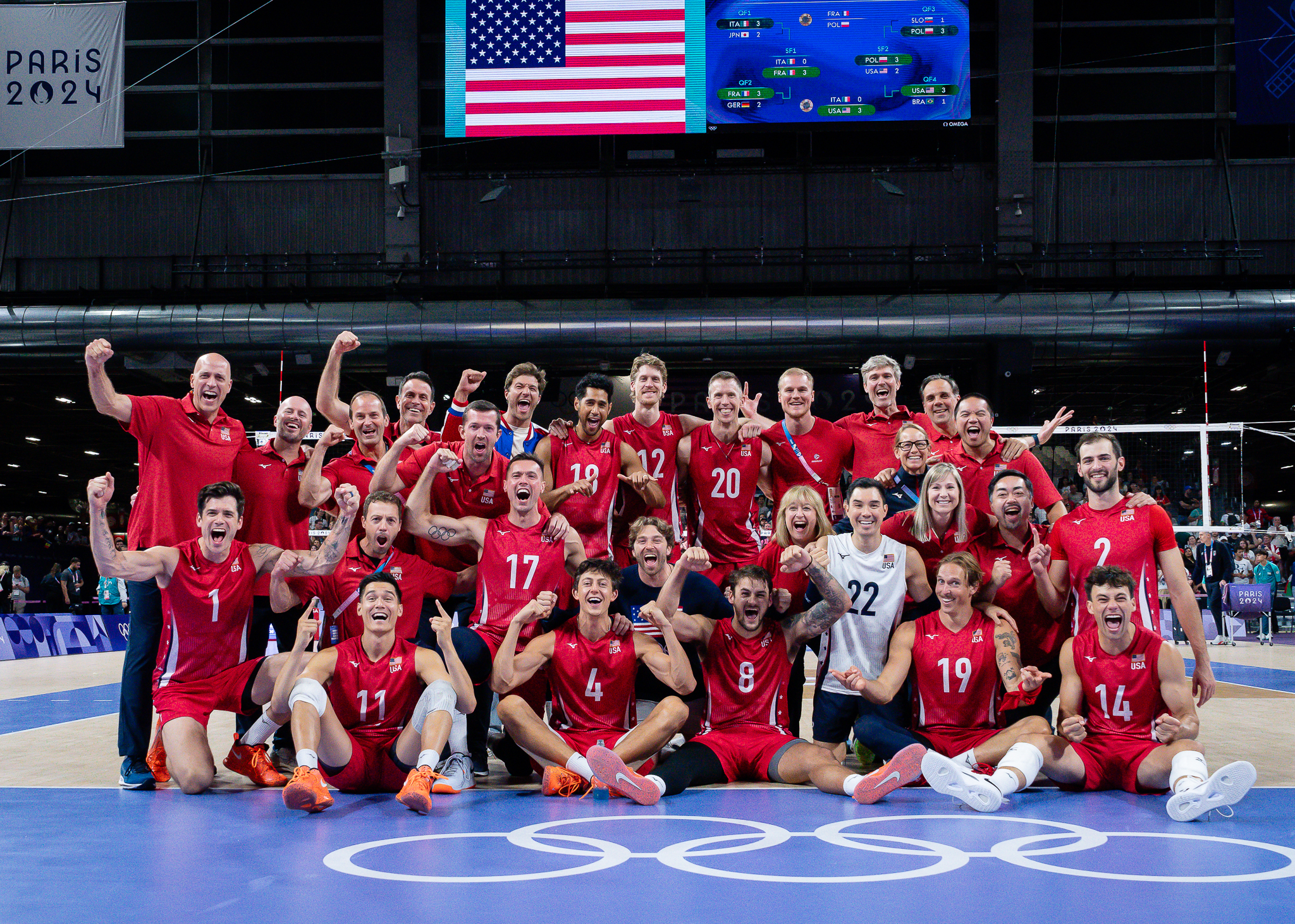 A group photo of Team USA men's volleyball in red uniforms pumping their fists in the air after winning bronze in Paris