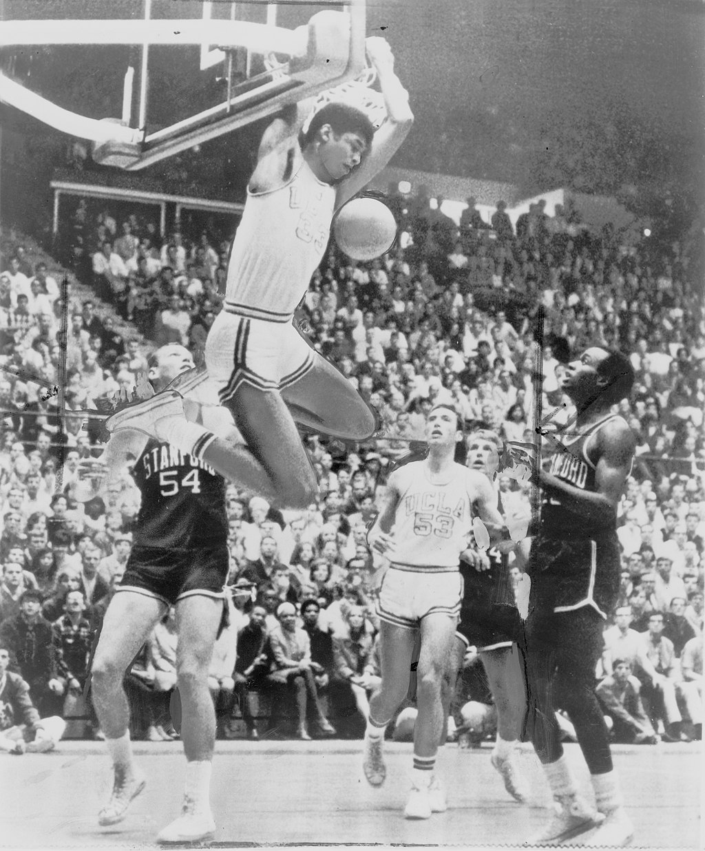 Kareem Abdul-Jabber reaches behind himself to dunk the basketball, looking down at three Stanford players