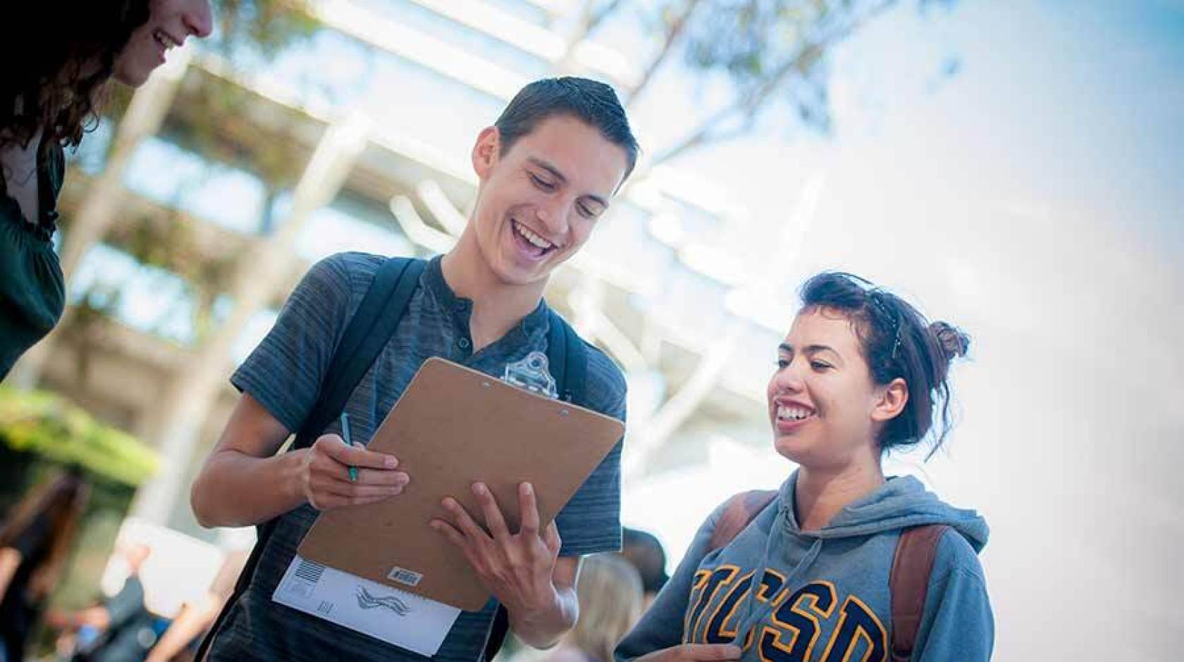 A student registers to vote on a clipboard, assisted by another student