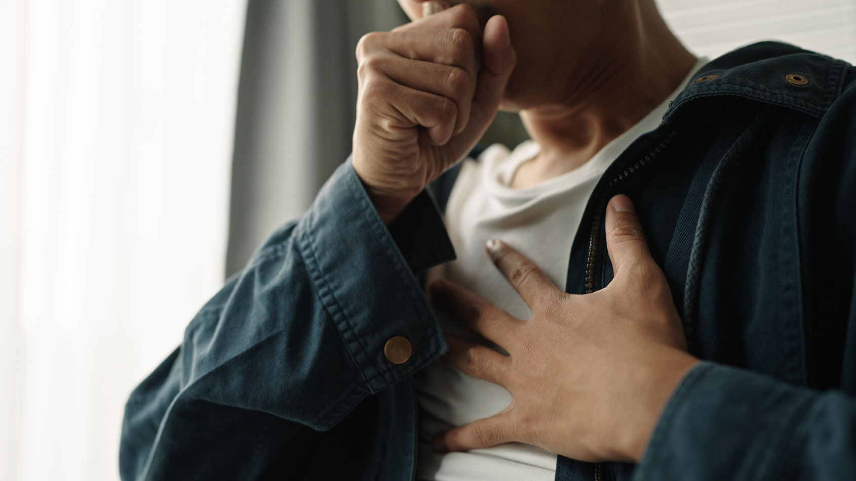 Man breathes into fist with his other hand over his chest