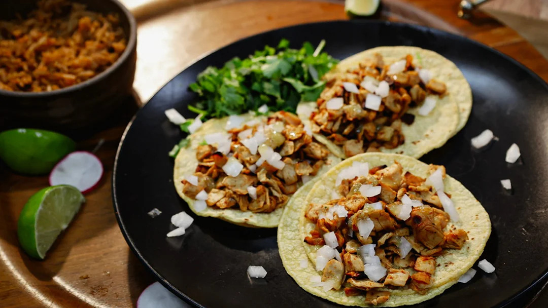 A platter of three tacos with onion and garnish