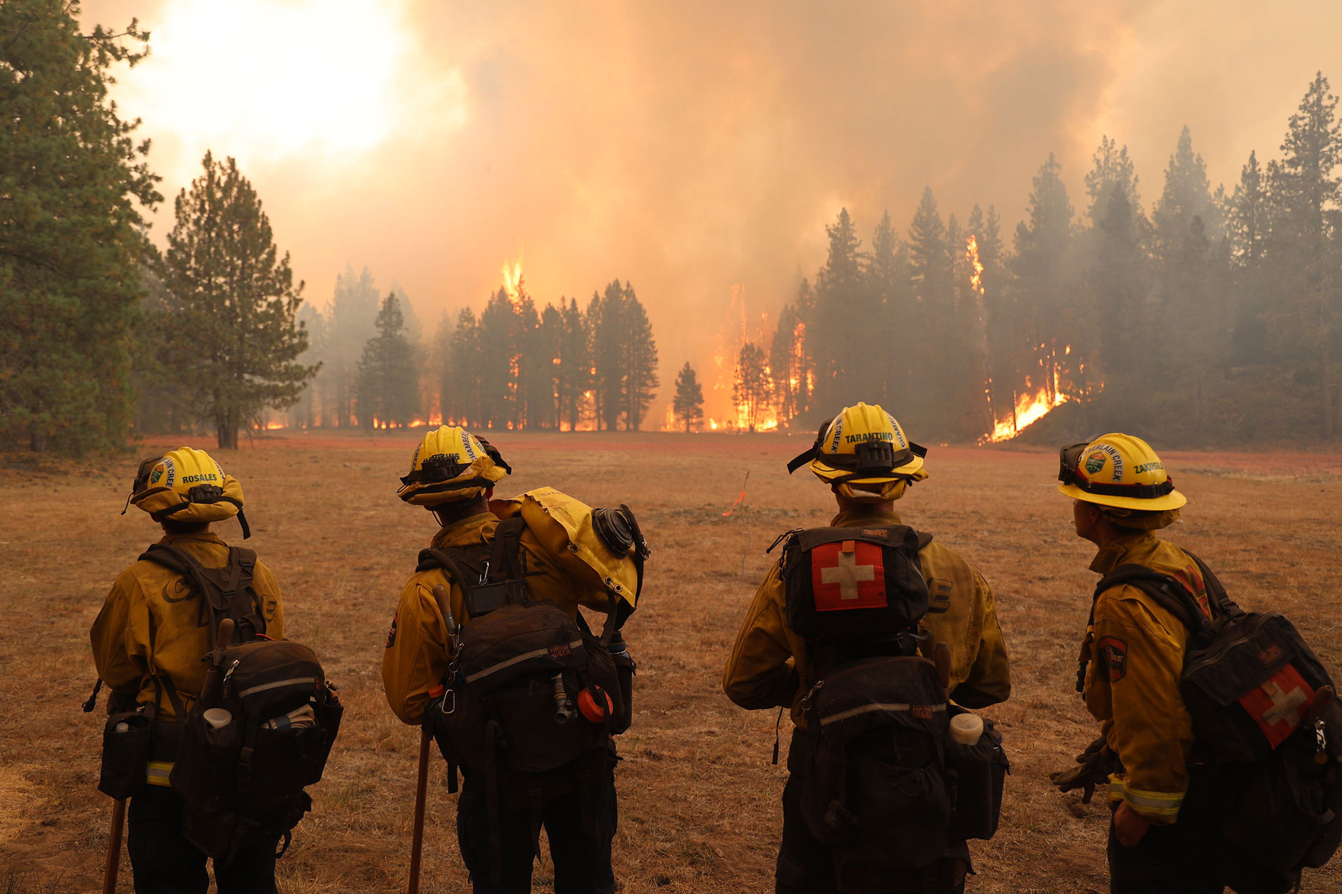 Four wildland firefighters keep watch on a fireline from across a field under smoky skies