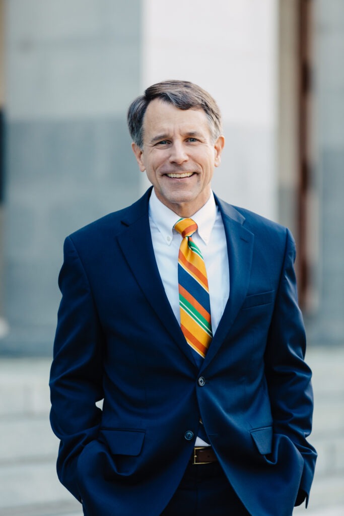 Dave Jones in a blue suit and striped tie, hands in pockets, smiles at camera