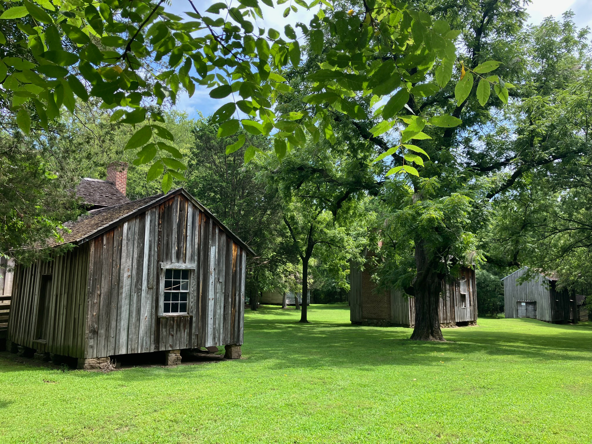 Old wooden cabins once used by enslaved people on a green lawn, trees among them