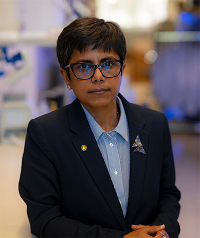 Woman with short dark hair and bangs, and large glasses, in a navy blue blazer